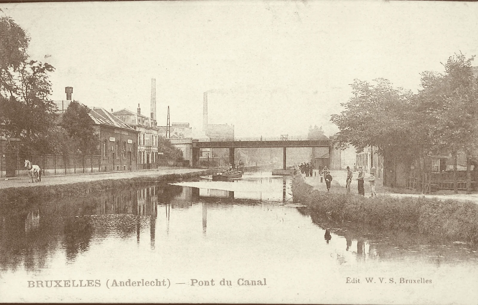 Carte postale ancienne du pont du canal à Anderlecht : usines et cheminées sur la rive gauche, une péniche sur l’eau, des promeneurs sur la berge