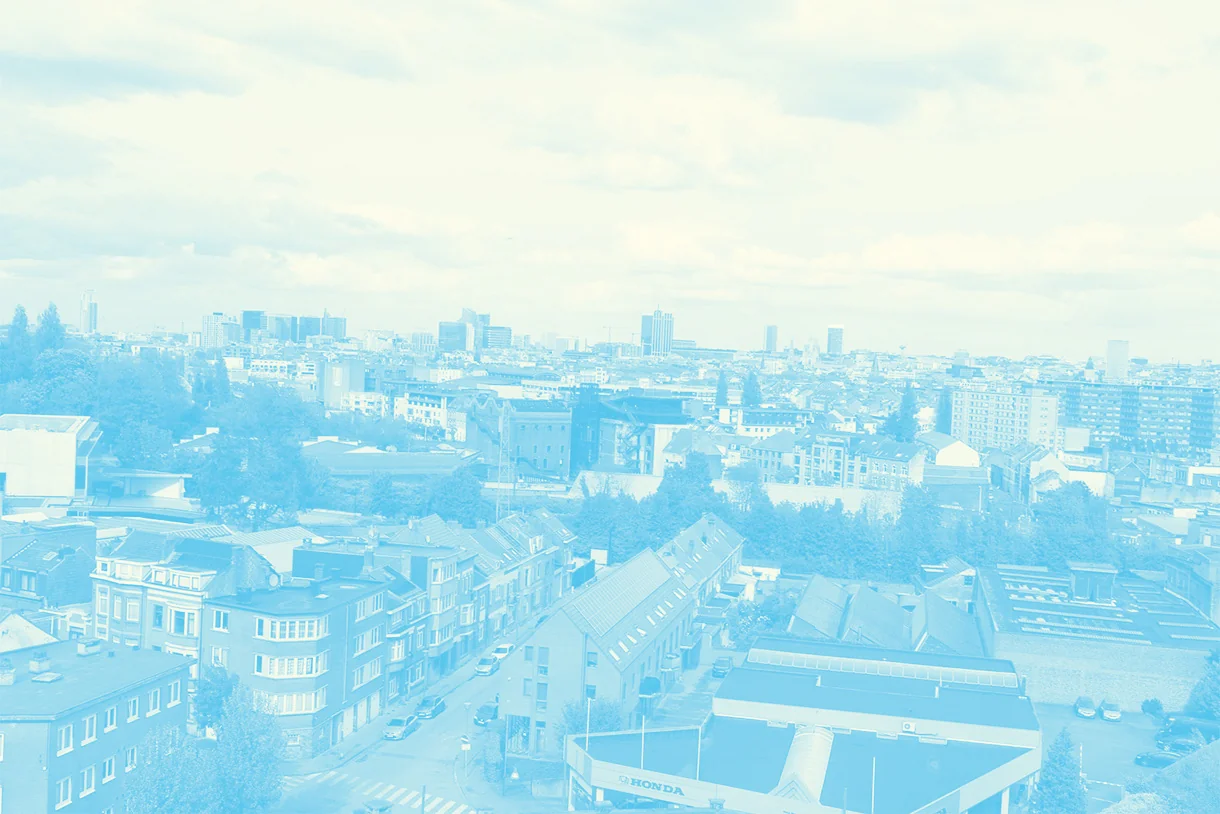 Vue panoramique sur les toits d’Anderlecht : immeubles et maisons serrés, quelques arbres, les tours de Bruxelles à l’horizon