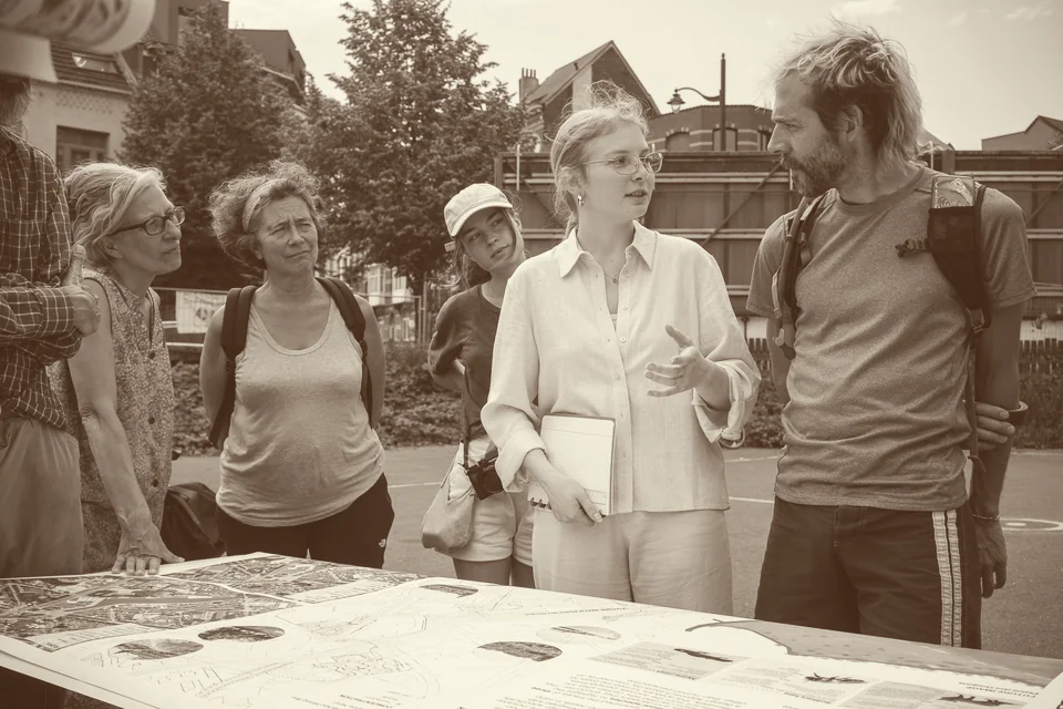 Atelier en plein air au marais : des habitantes et des habitants discutent debout autour d’une table couverte de plans du site