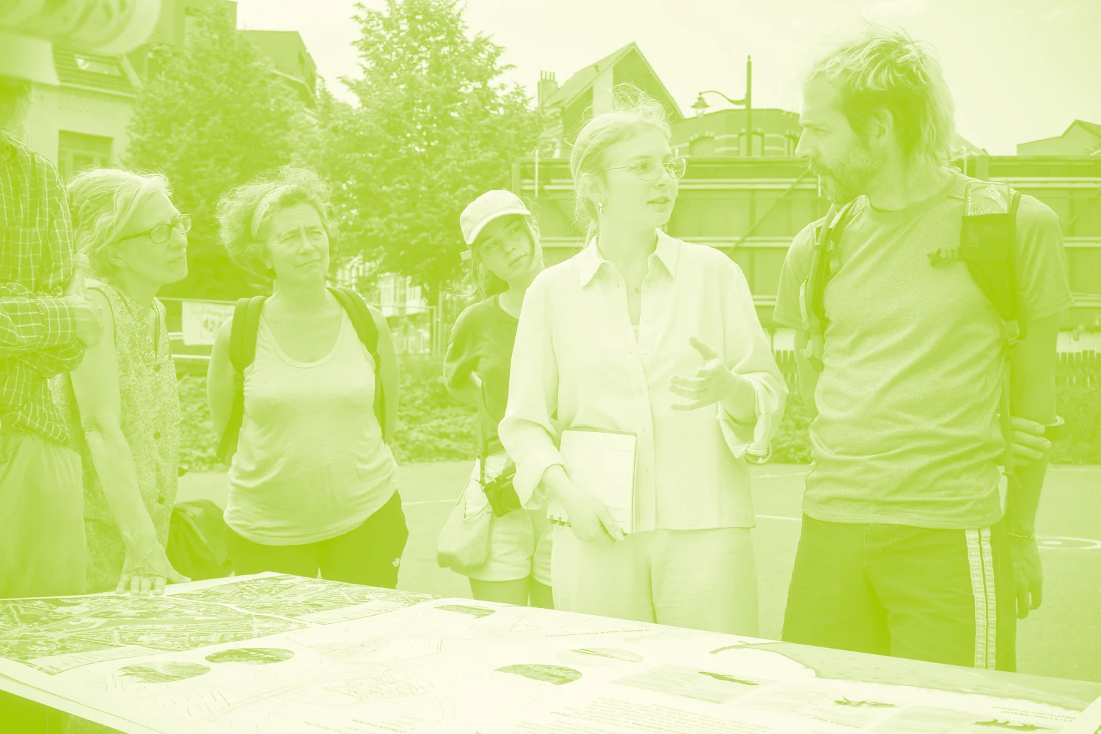 Atelier en plein air au marais : des habitantes et des habitants discutent debout autour d’une table couverte de plans du site